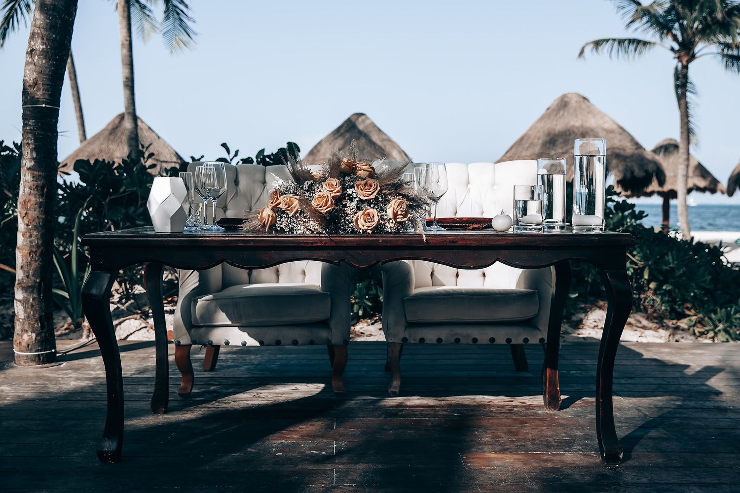 Beachfront wedding venue with thatched roof palapas and palm trees along the shoreline.