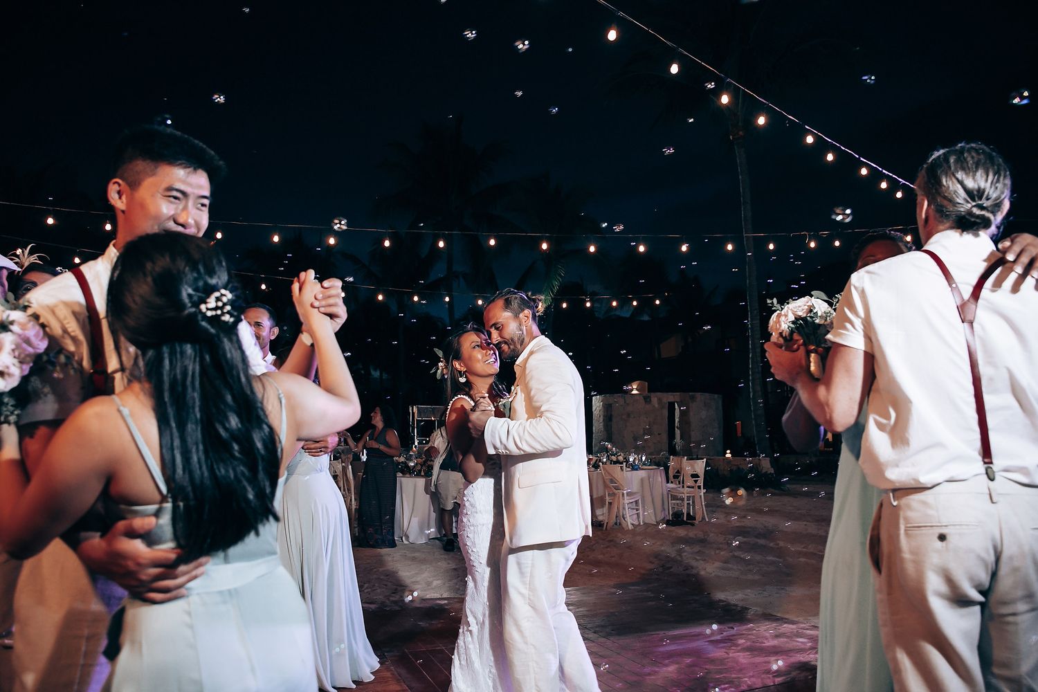 Wedding reception dance floor under string lights with guests celebrating at night.