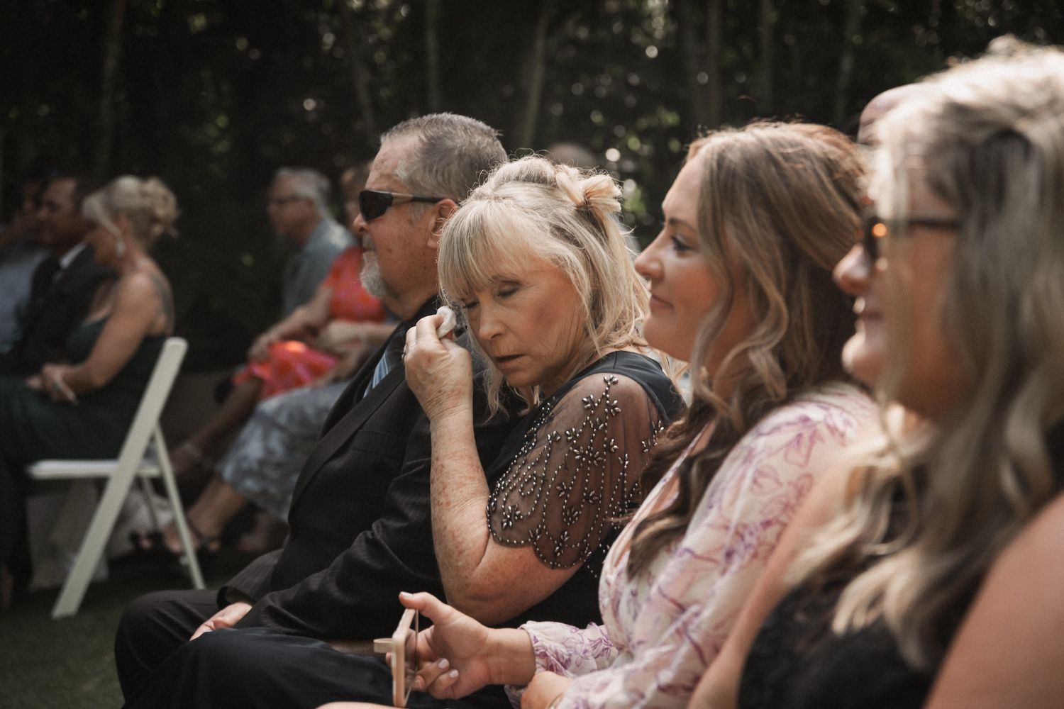 Emotional wedding guest wiping tears during outdoor garden wedding ceremony.