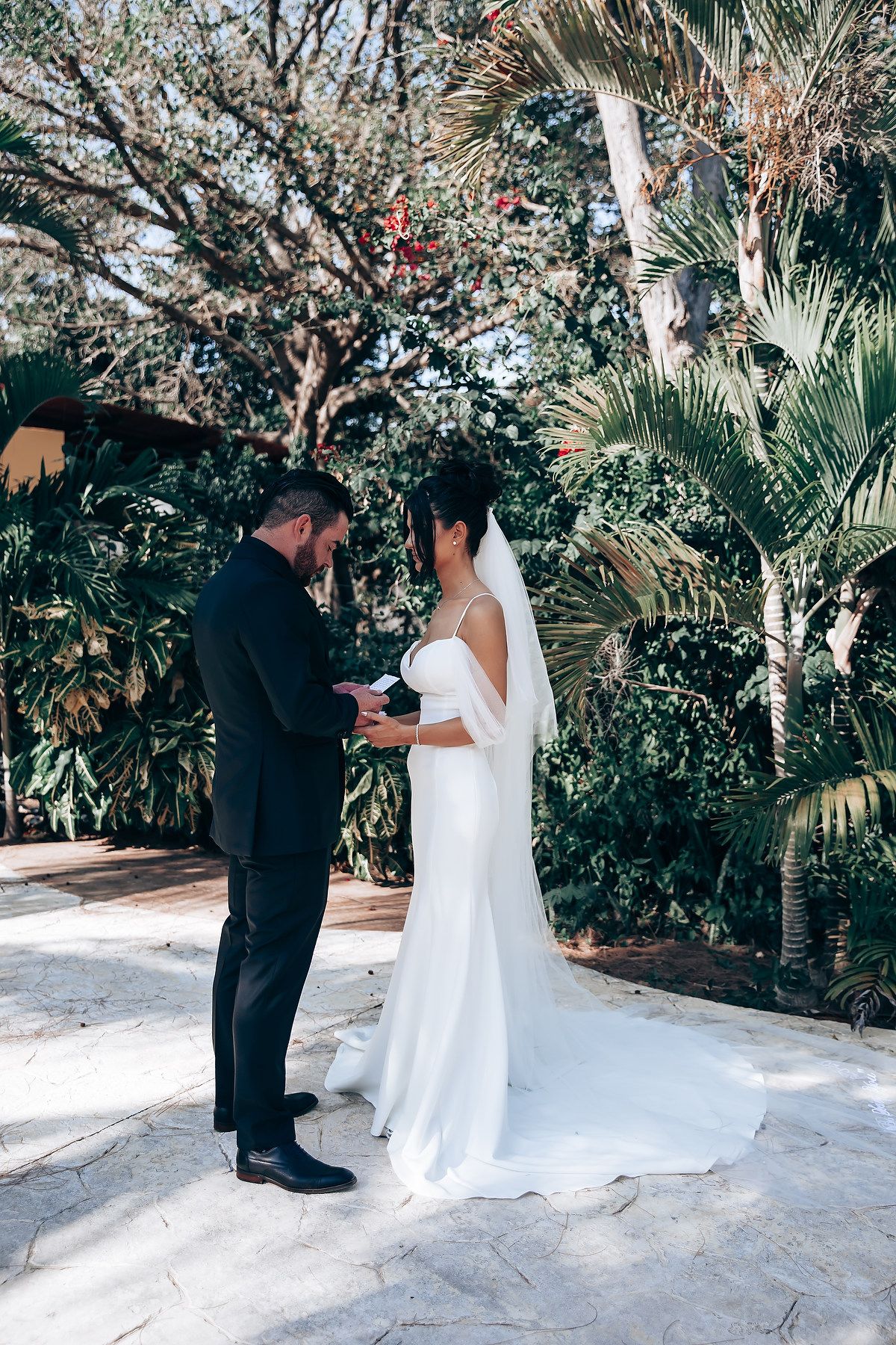 First look wedding moment captured in a lush tropical garden setting with palm trees.
