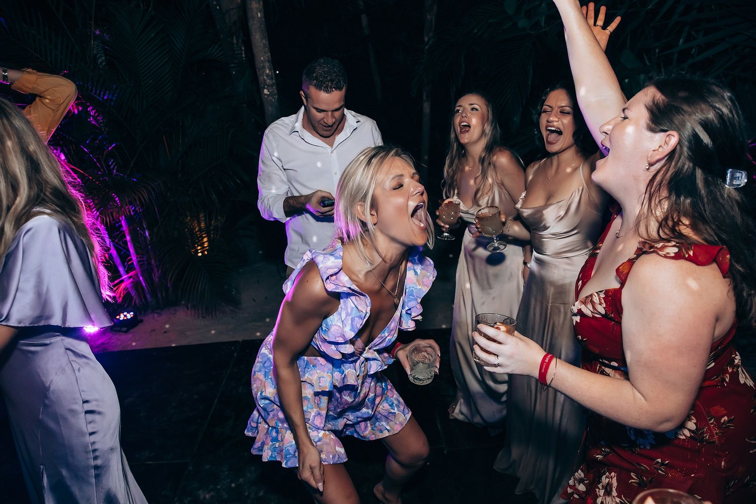 Dance floor filled with guests celebrating at nighttime wedding reception with purple lighting.