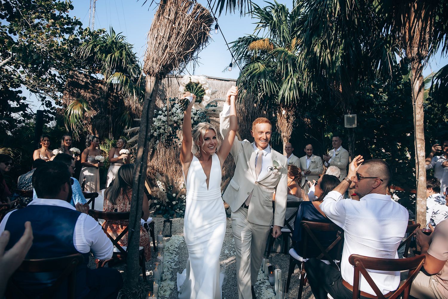 Wedding guests celebrate outdoors under palm trees during a joyful ceremony.