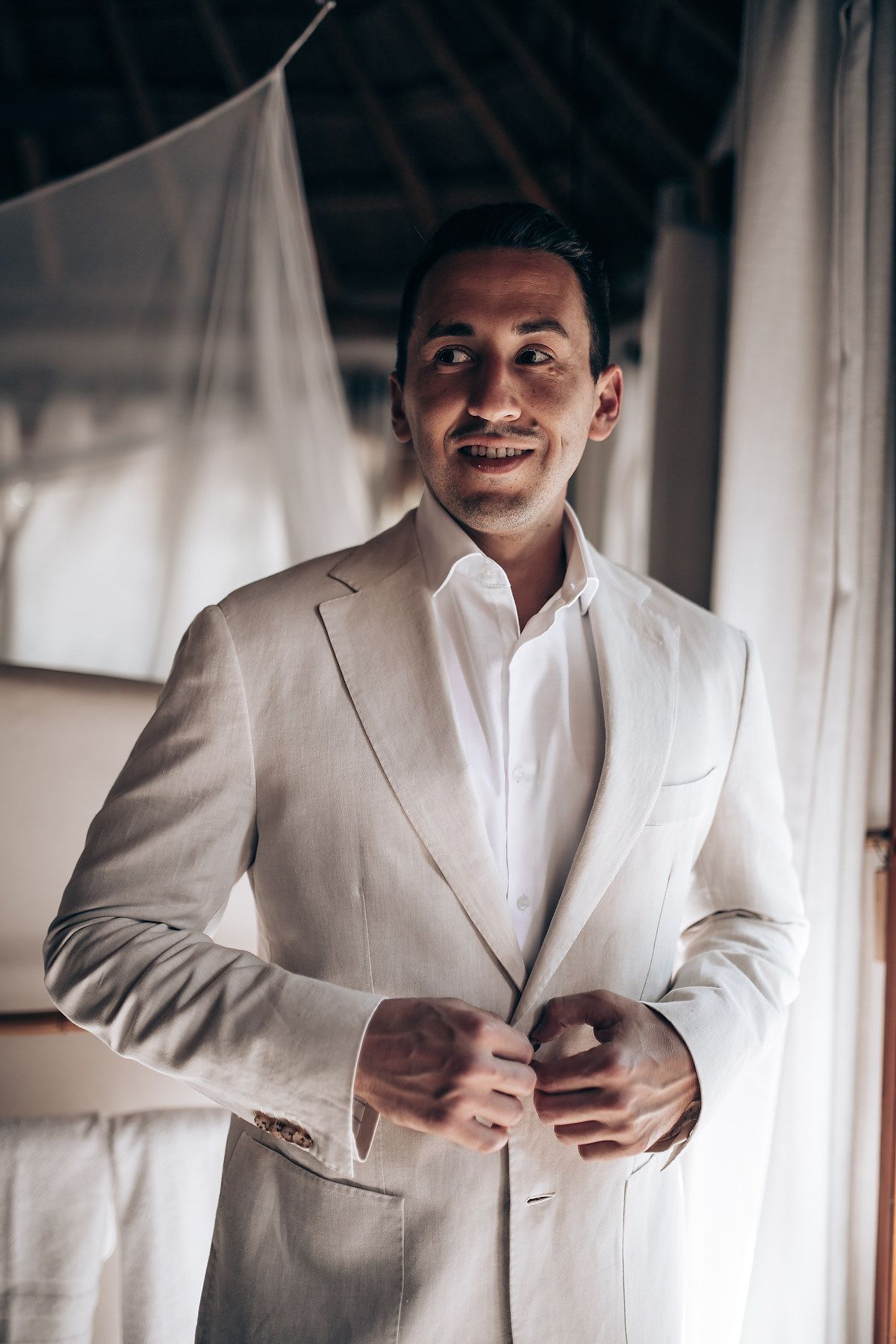 A person wearing a crisp white suit jacket and dress shirt smiles while getting ready.