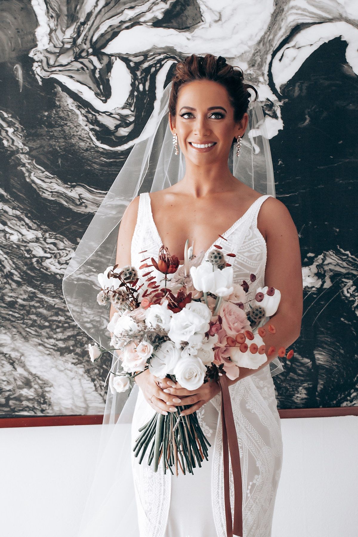 Elegant bridal bouquet featuring white roses and burgundy accents against a marbled black and white backdrop.