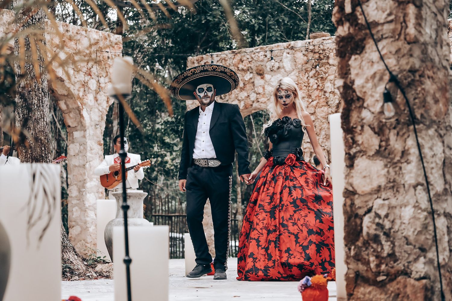 A couple in Day of the Dead inspired formal wear stands in front of stone archways.