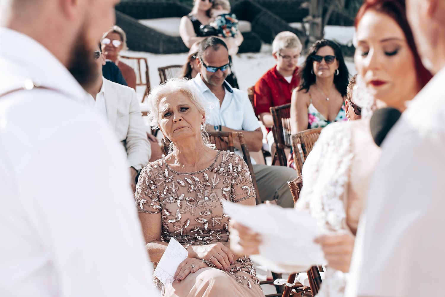 Wedding guests gather outdoors for a ceremony with white chairs and floral decorations.