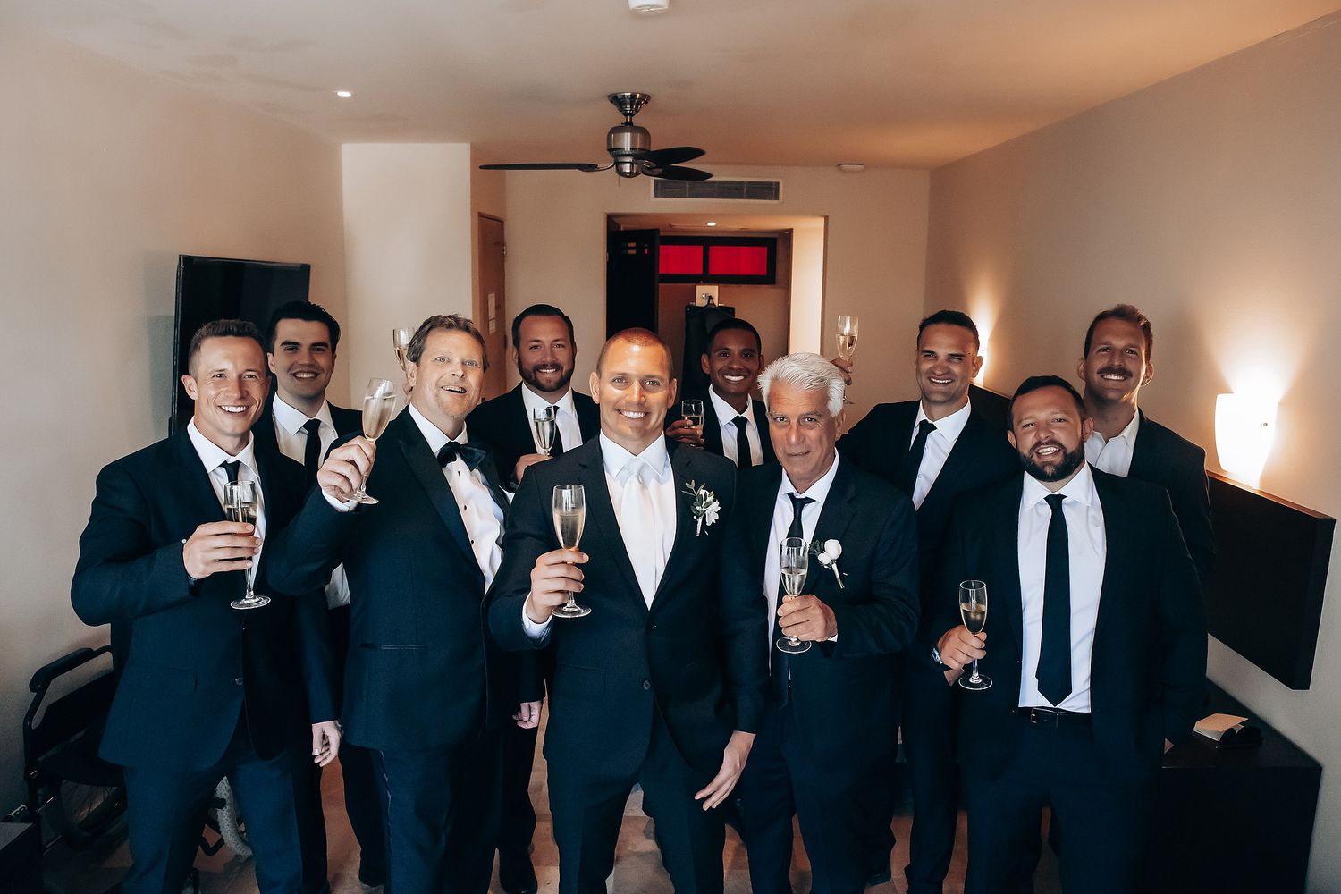 Groomsmen in black suits raising glasses for a celebratory toast.