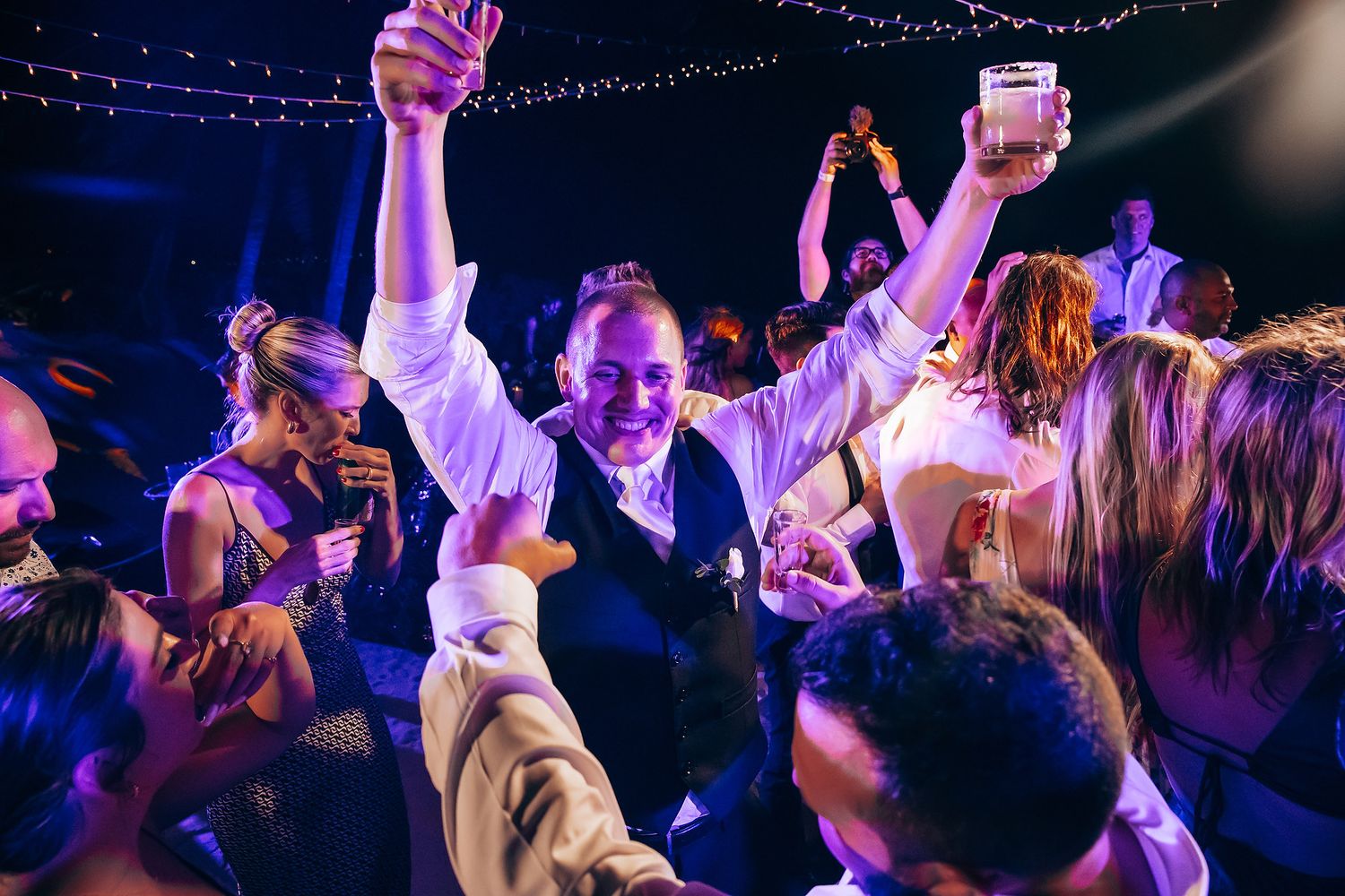 Wedding reception dance floor illuminated with purple lighting and string lights overhead.
