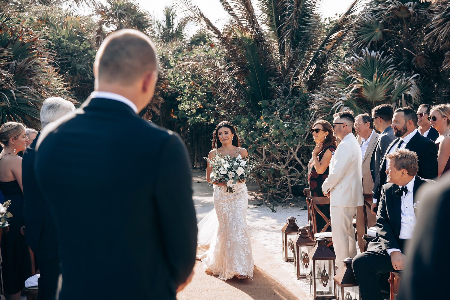 Wedding ceremony guests seated outdoors beneath trees and natural greenery.