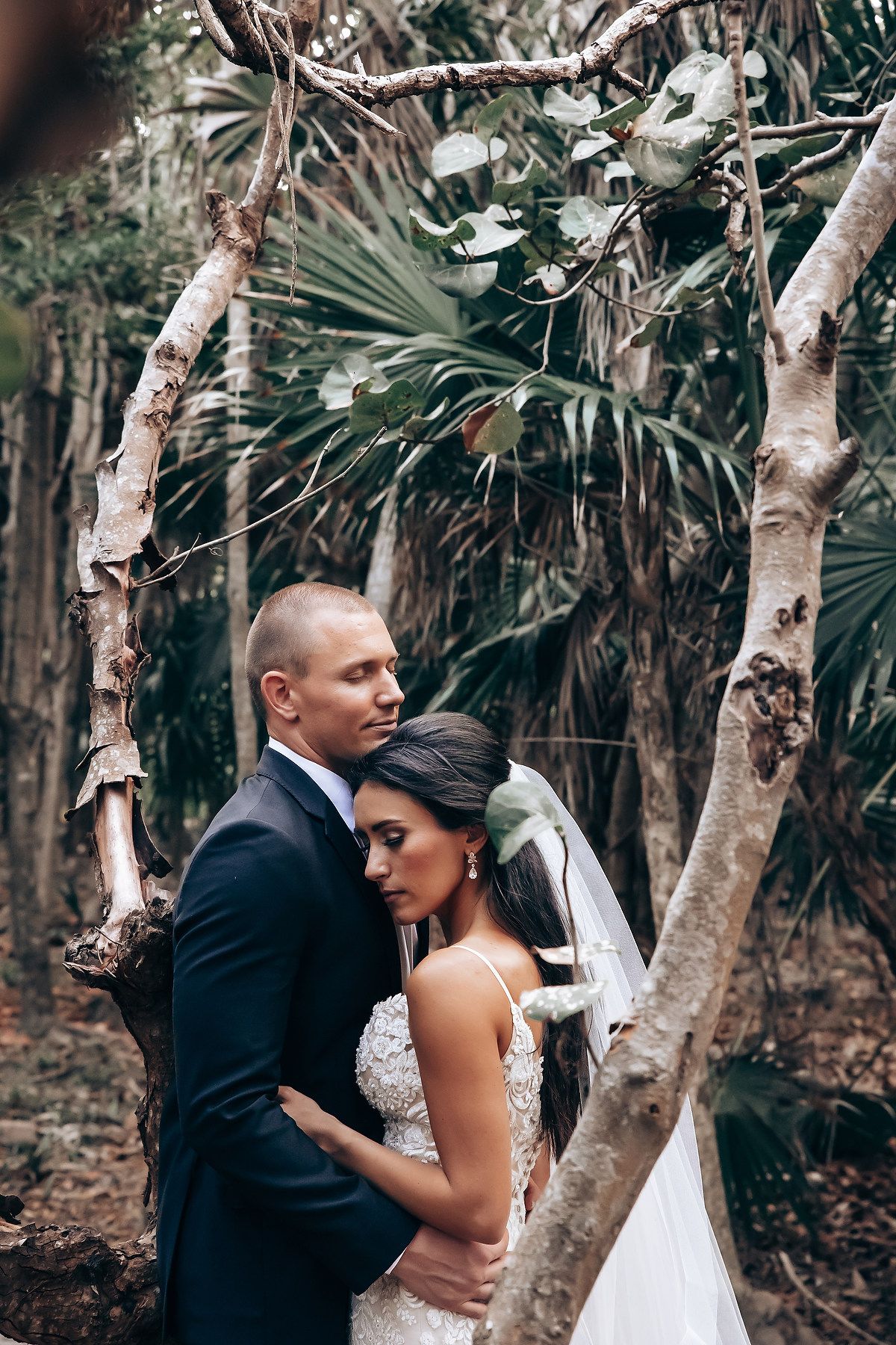 A romantic moment captured between a couple in formal attire among palm trees and natural greenery.