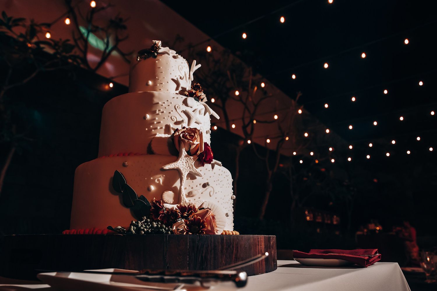 Elegant white wedding cake displayed under romantic string light ambiance.