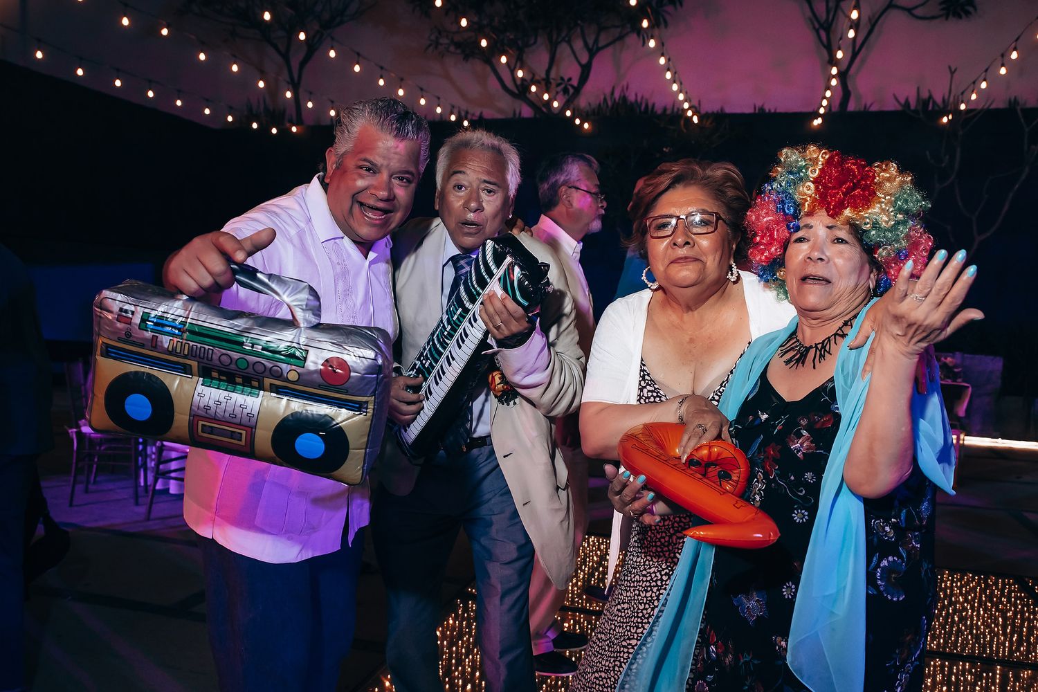Party guests having fun with retro props under string lights at night.