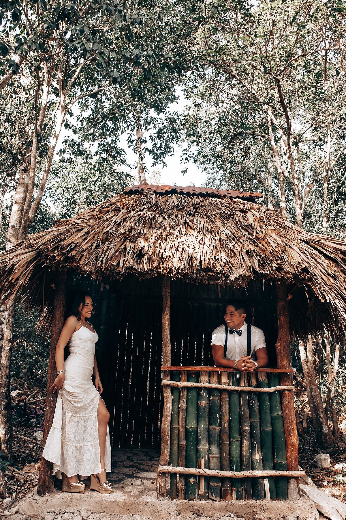 A rustic wooden hut with thatched palm roof stands among trees in a tropical setting.