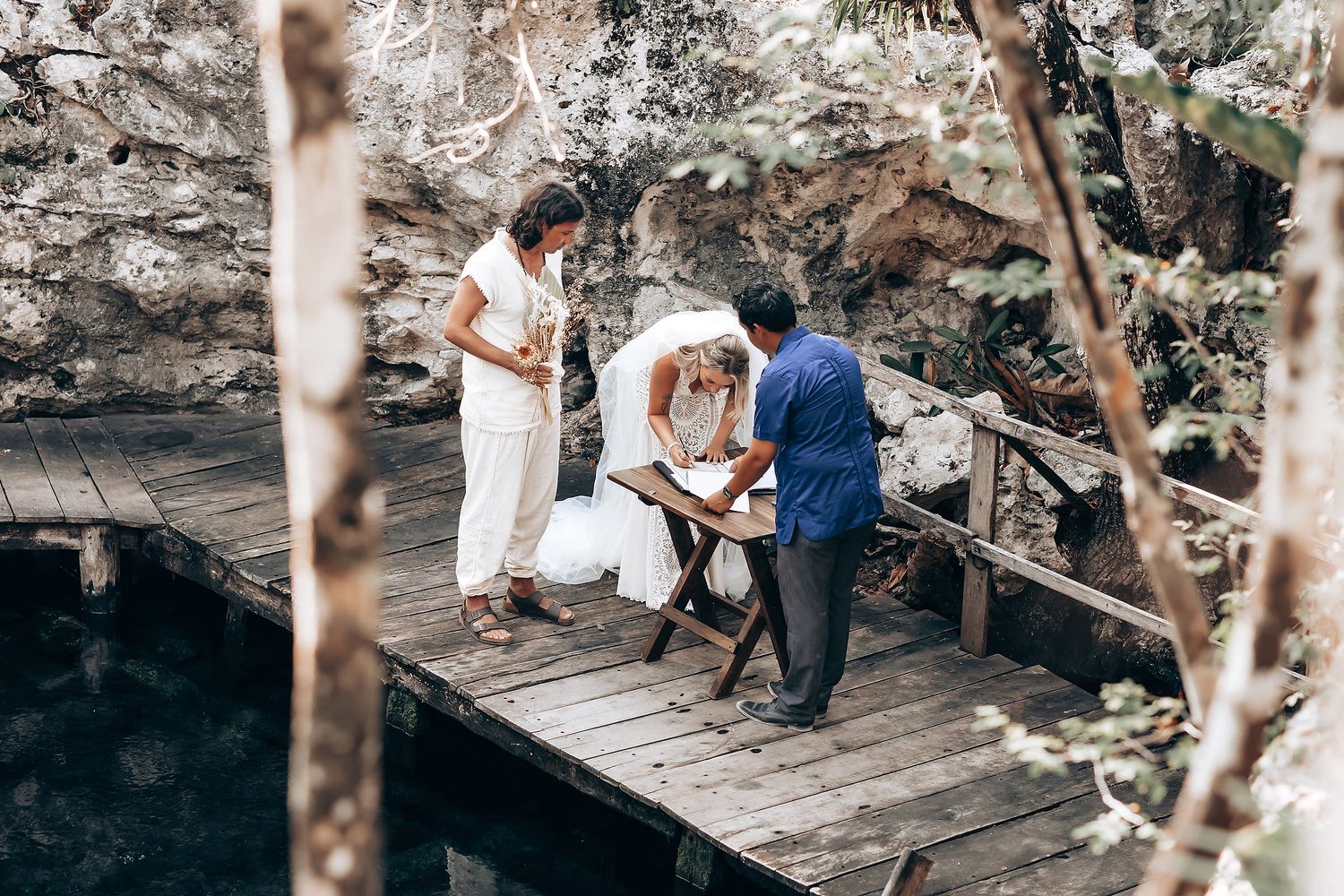 A couple sits together on a rustic wooden deck surrounded by trees in a natural outdoor setting.
