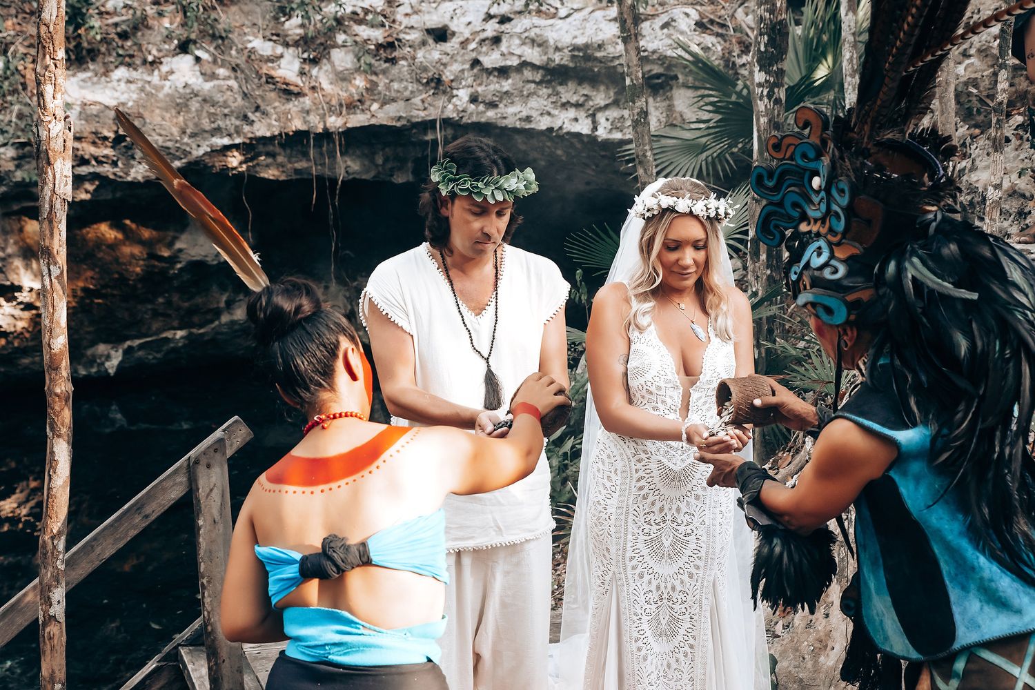 Wedding party in white attire poses together in a tropical setting with palm fronds and rock formations.