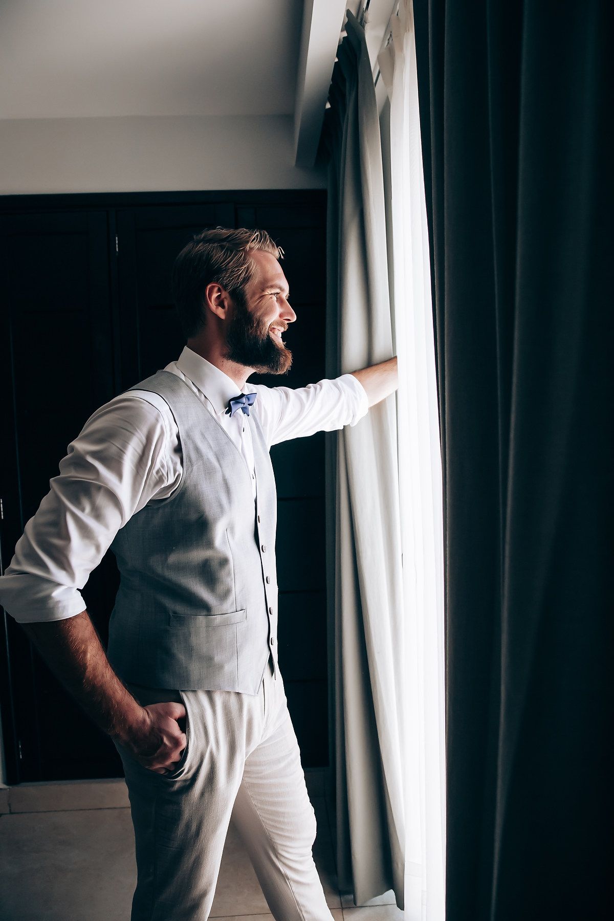 A figure in a white dress shirt and dark bowtie gazes thoughtfully through a window in a dramatic black and white series.