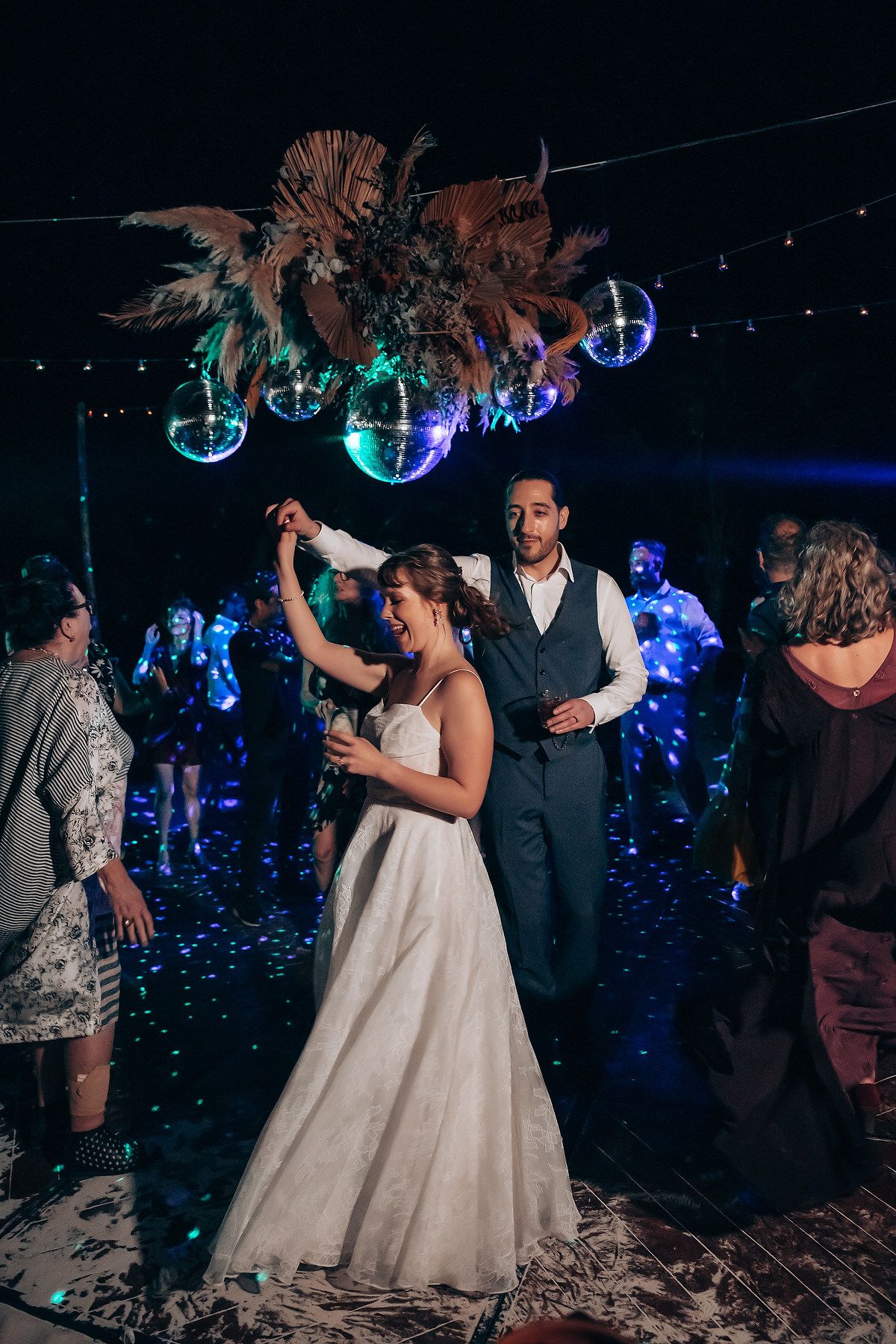 Wedding party dancing under blue disco lights and glowing orbs during an evening reception celebration.
