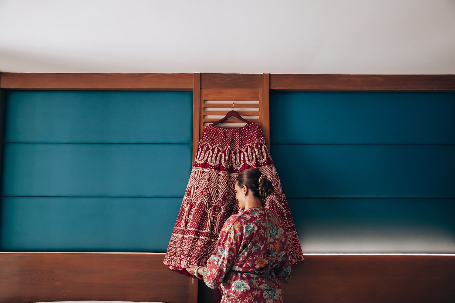 Red traditional Indian dress hanging against turquoise blue wall panels.