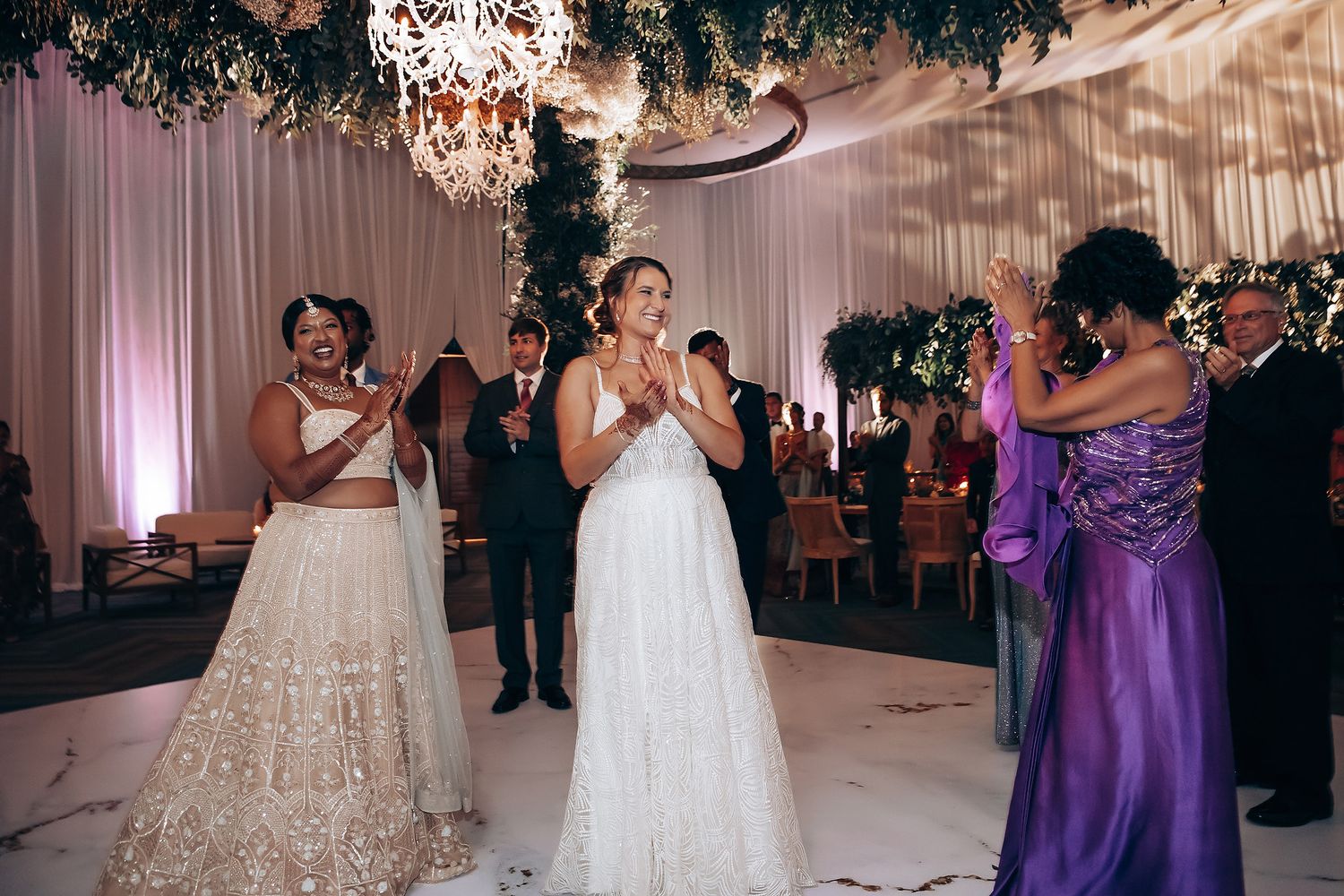 Indoor wedding reception with elegant decor featuring greenery and purple lighting.