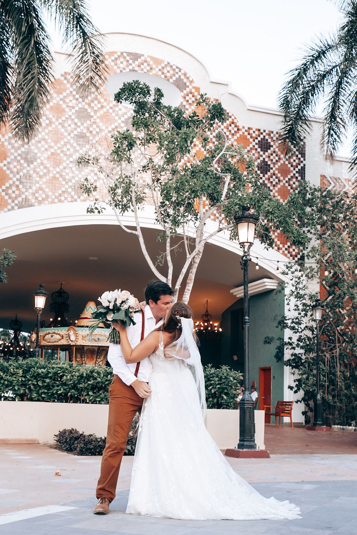 Couple in wedding attire performs romantic dance moves under decorative outdoor archway.
