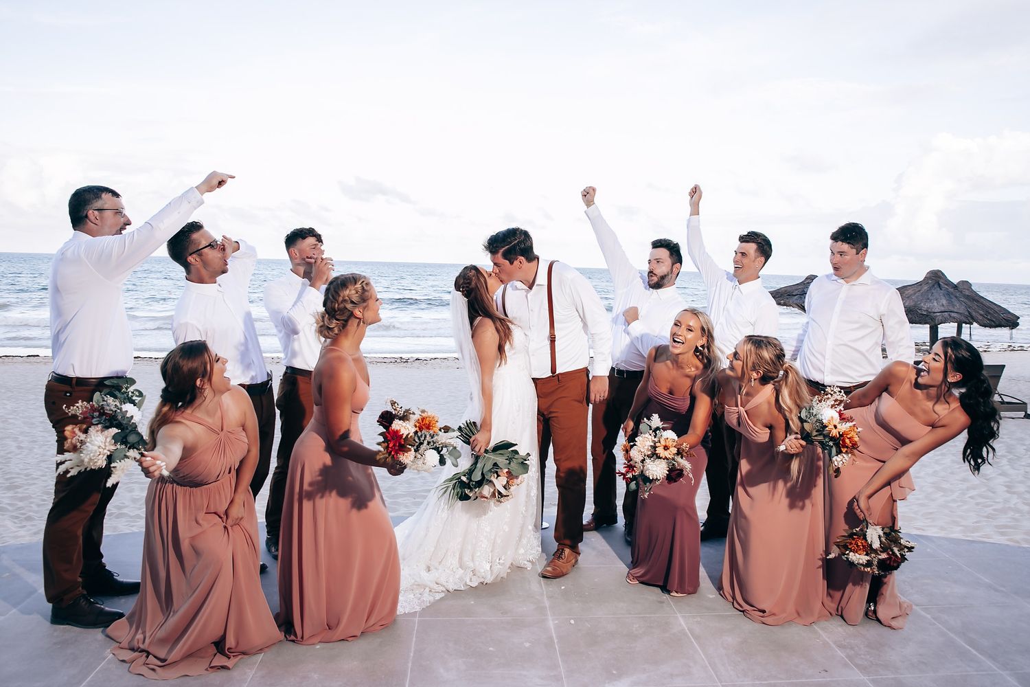 Wedding party in brown dresses posing together on sandy beach.