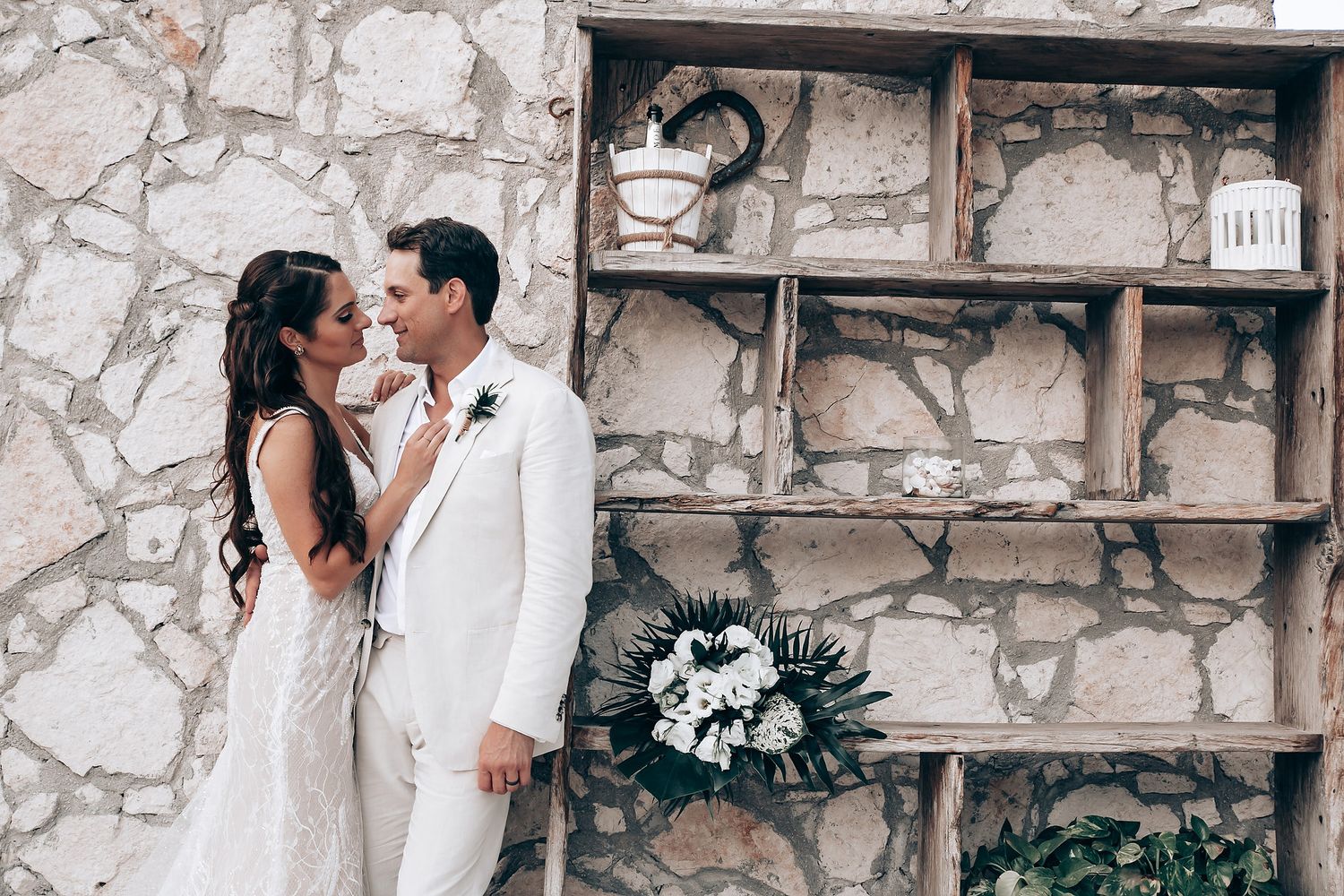 Intimate moment between couple against stone wall with rustic wooden shelves.