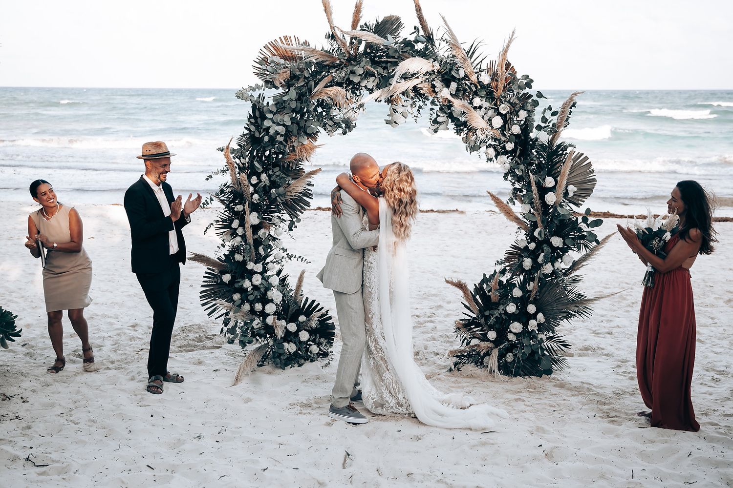 A beach wedding ceremony under a floral arch with ocean waves in the background.