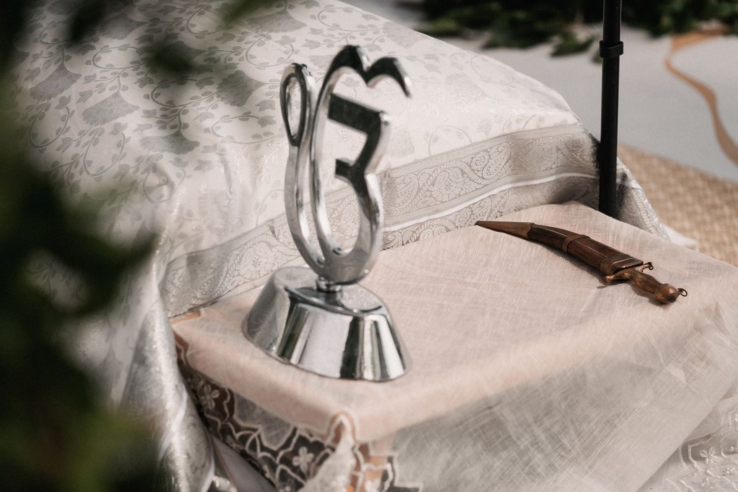 Silver Ik Onkar symbol and ceremonial kirpan on decorated cloth at Sikh wedding.