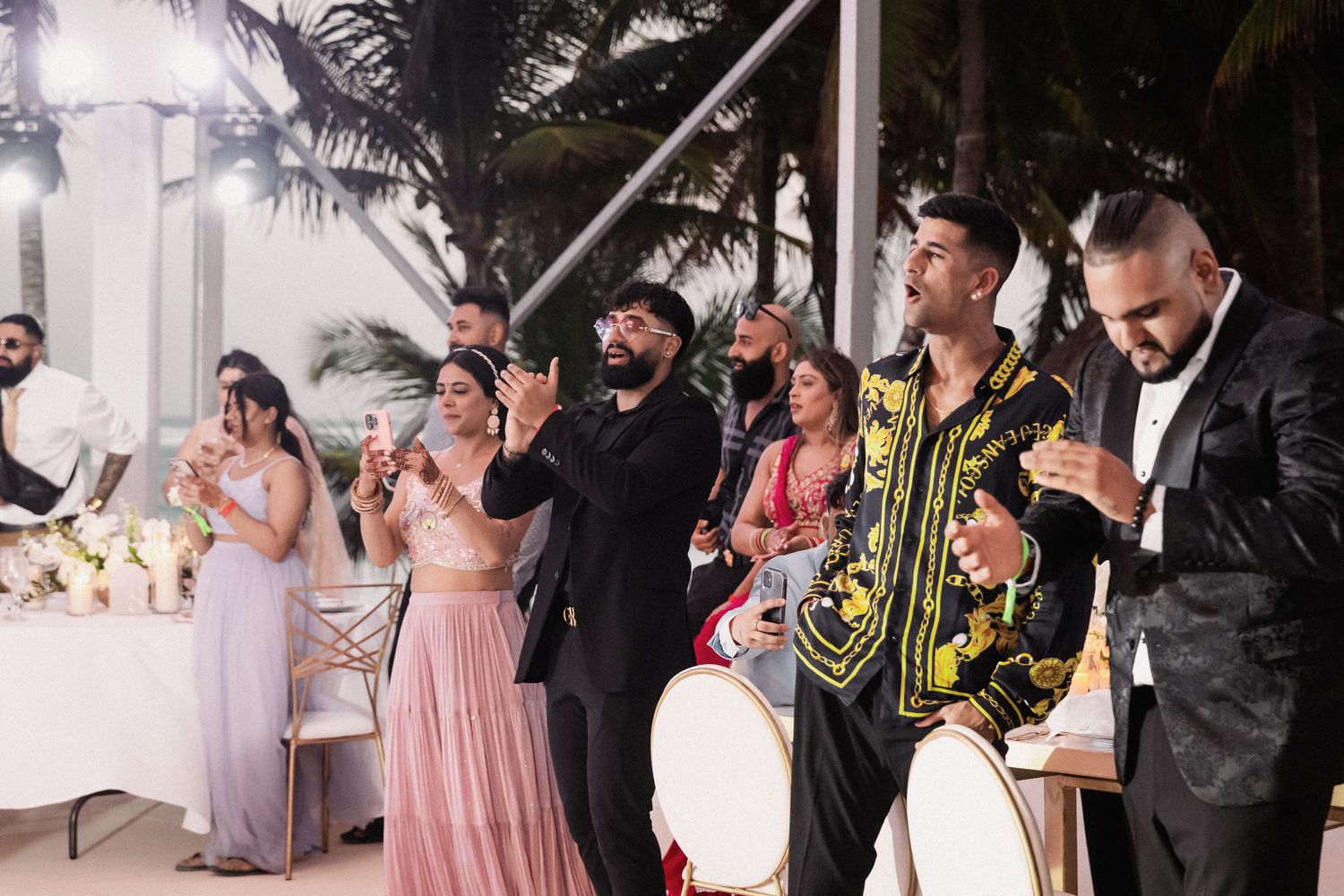 Wedding guests celebrating and clapping at evening tropical outdoor reception.