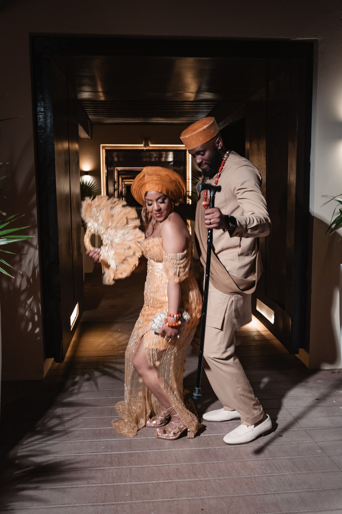 Couple in elegant Nigerian traditional wedding attire posing in warmly lit hallway.
