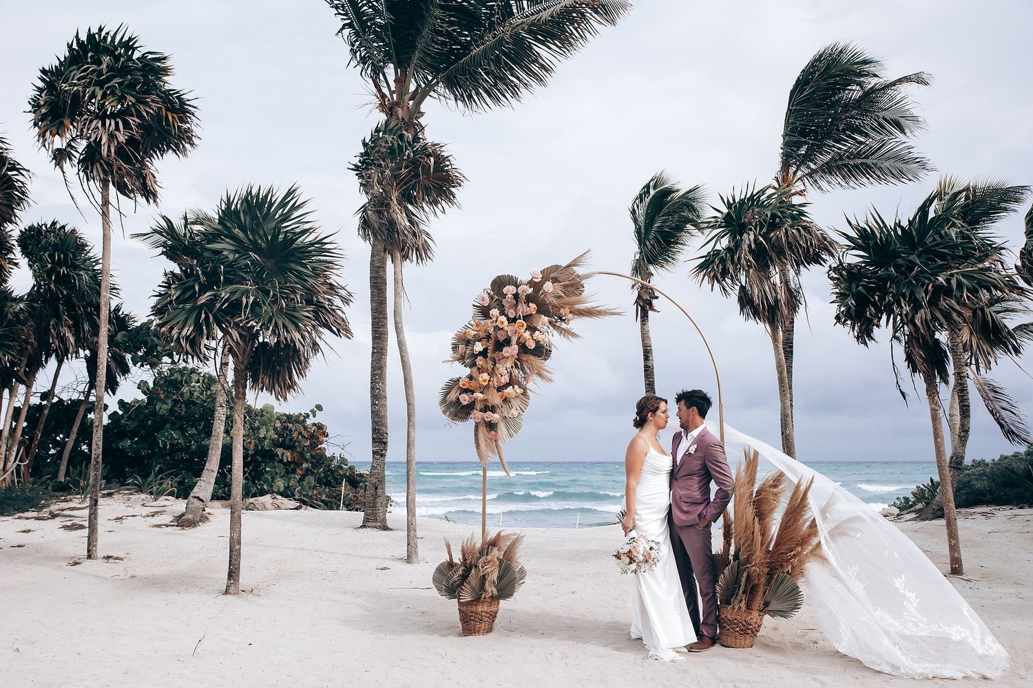 A beachside wedding ceremony with palm trees and white chairs against an ocean backdrop.