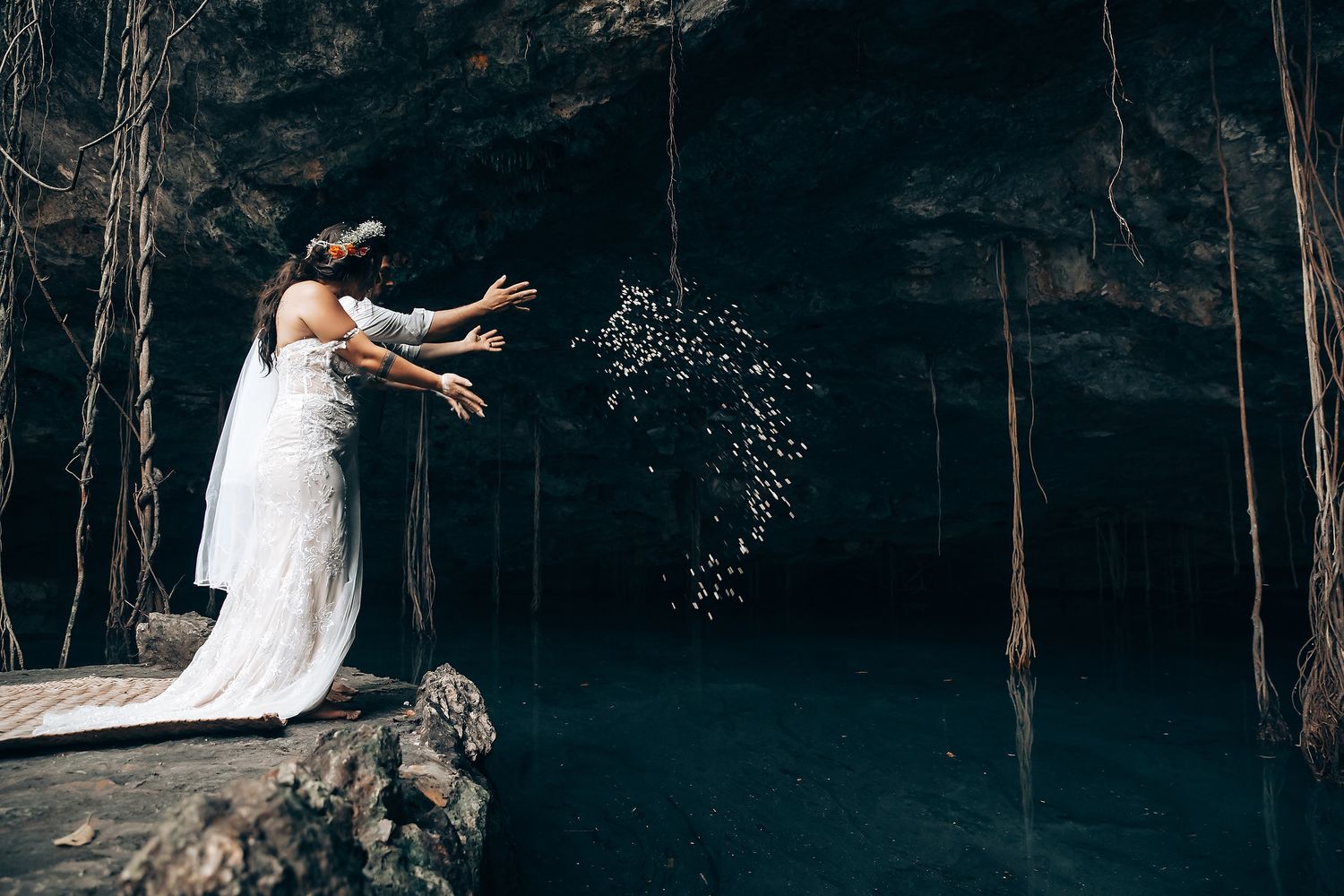 A couple in wedding attire poses for romantic photos in a scenic cave setting.