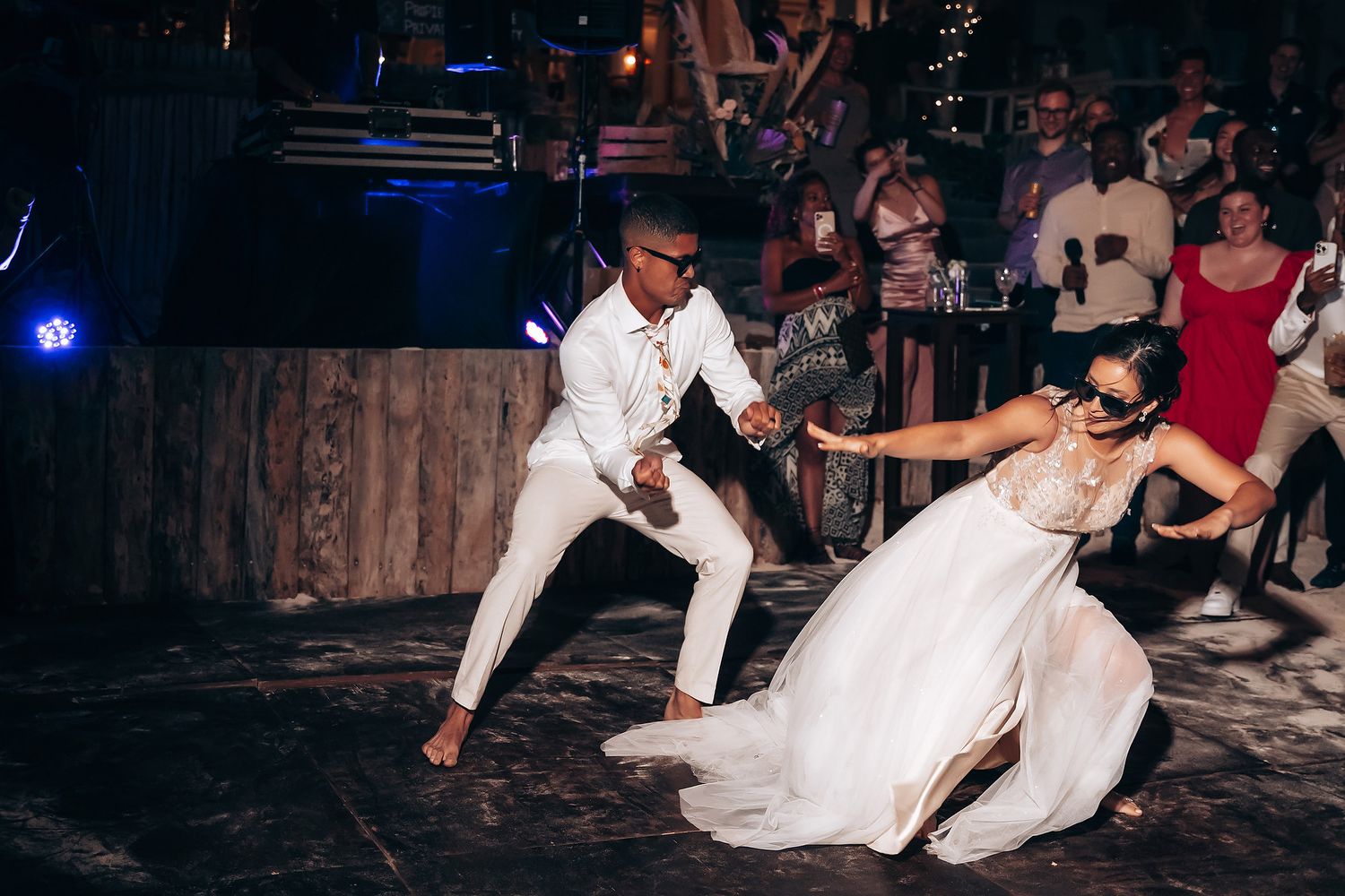 Wedding party dancing and celebrating during nighttime reception under outdoor lighting.