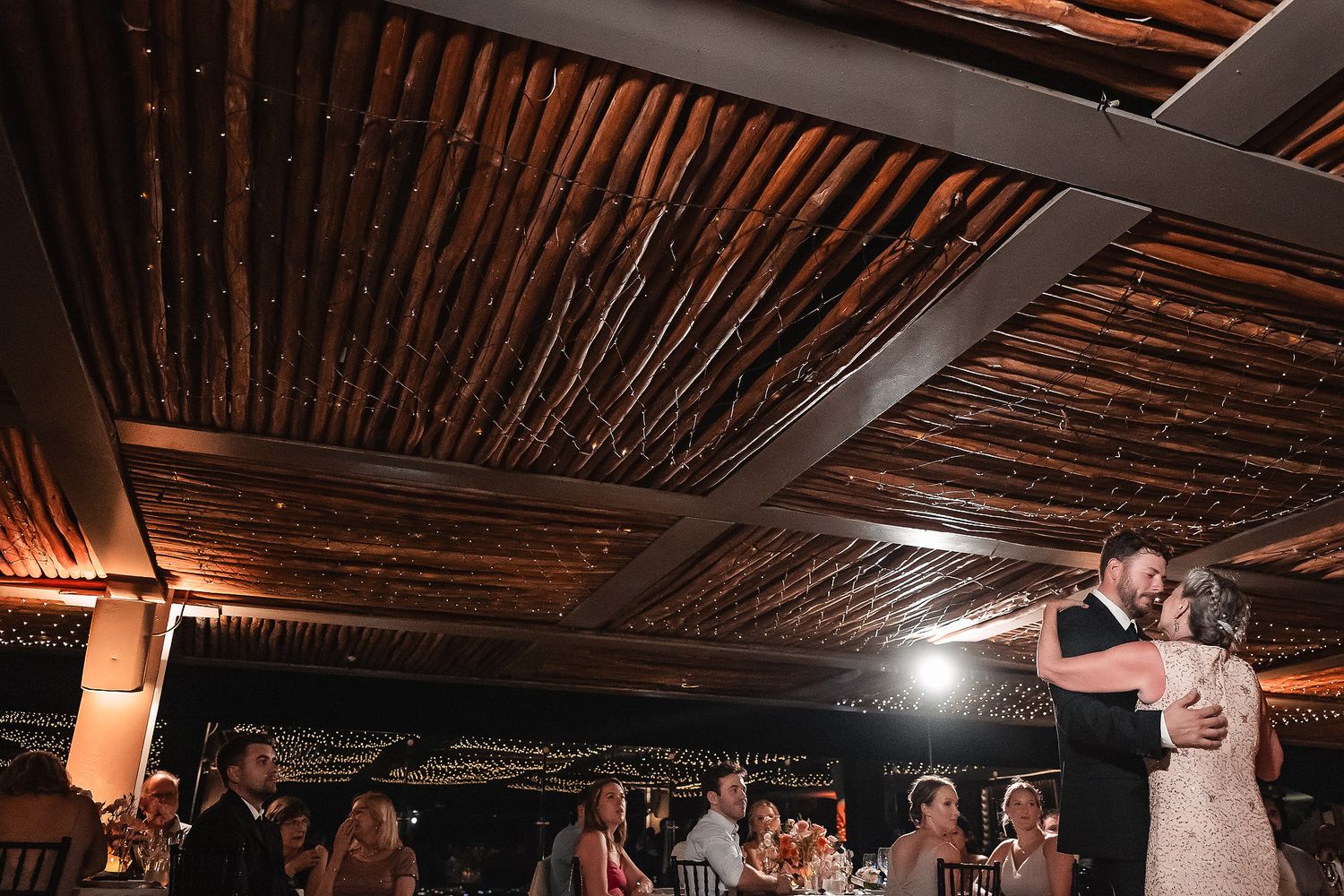 Wedding reception venue features rustic wooden ceiling beams and ambient lighting.