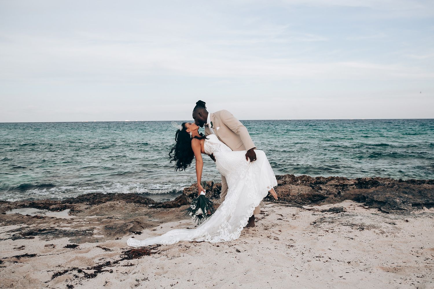Wedding couple posing on scenic beach with ocean waves in background.