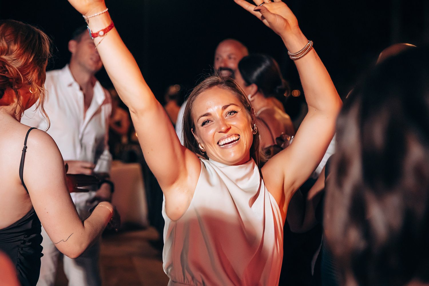 Person dancing with arms raised in a white top at a nightclub party with crowd in background.