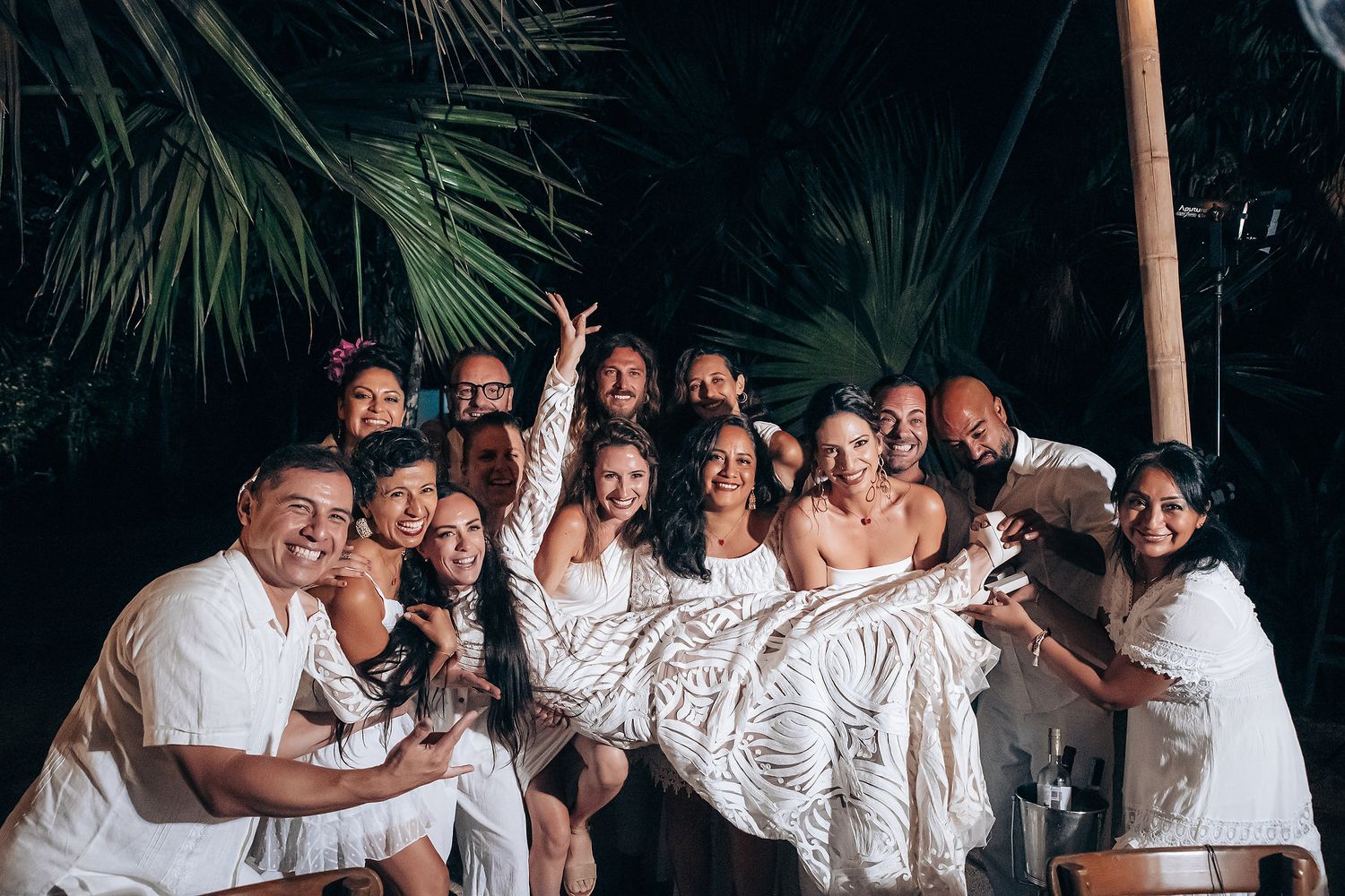 Group of wedding guests wearing white outfits dancing and celebrating together at a party.