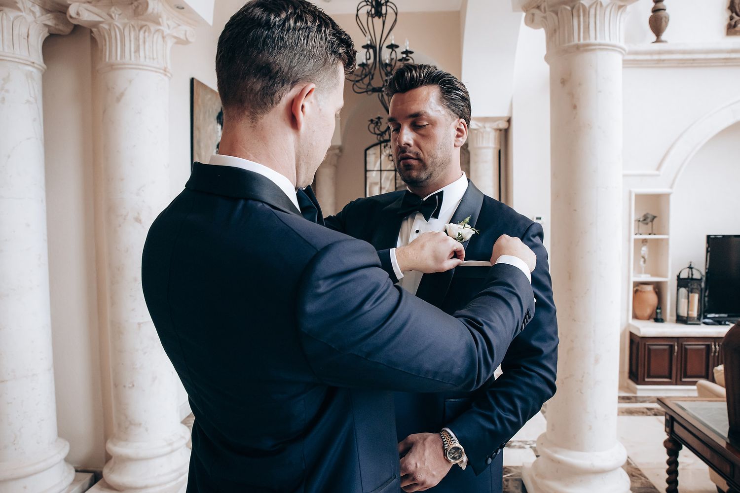 Two people in formal attire dance together in an elegant venue with white columns and ornate architectural details.