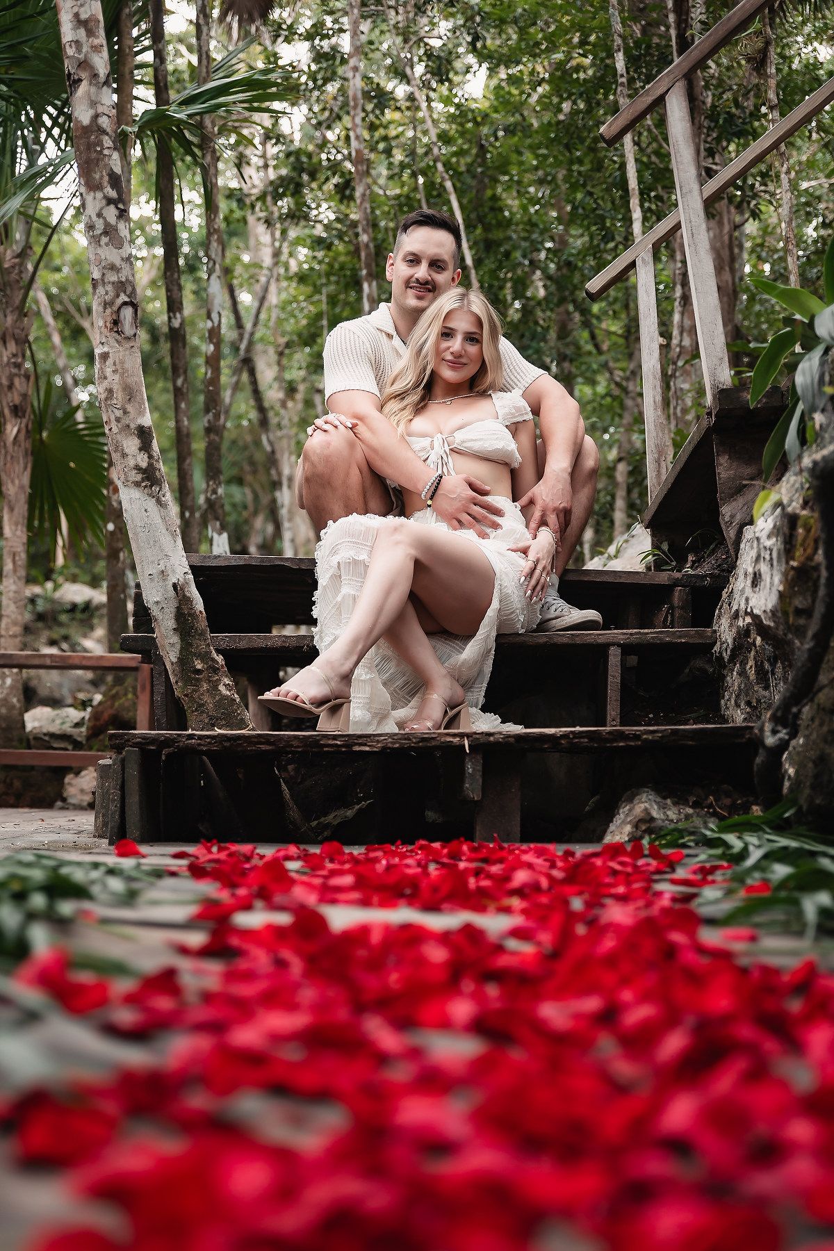 Romantic scene on wooden steps with red rose petals scattered below.