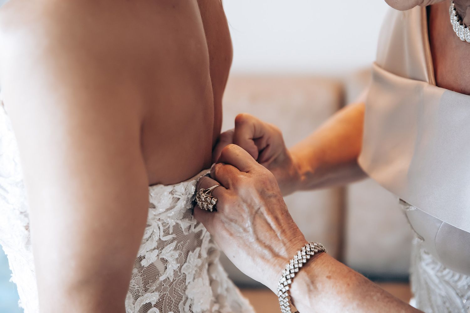 Wedding preparations show hands adjusting a delicate white lace dress with intricate beading and details.