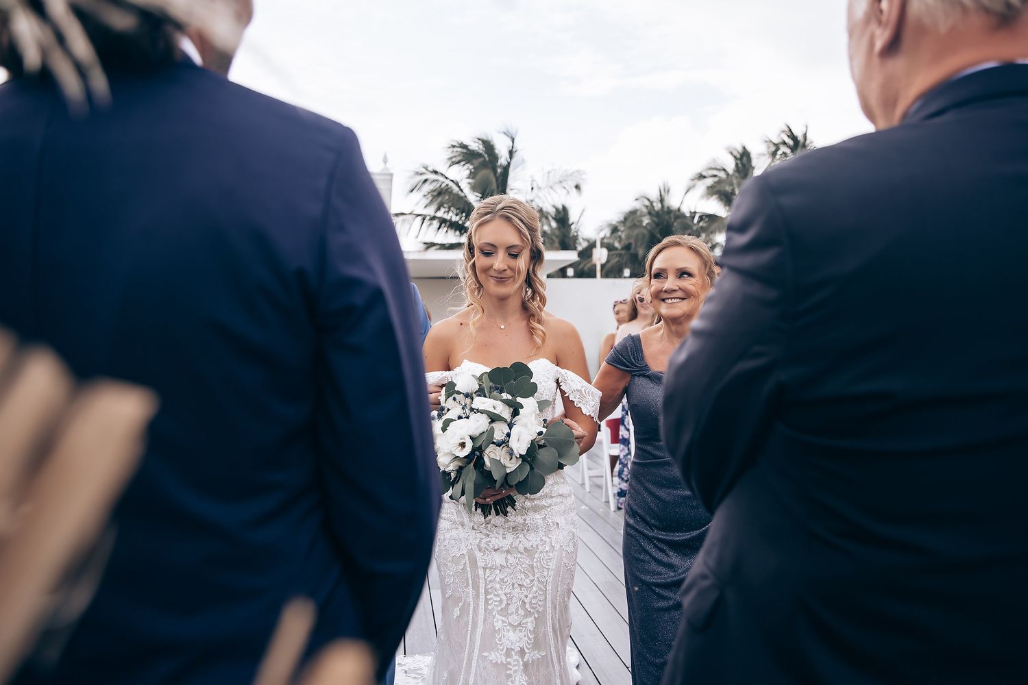 Wedding ceremony guests gather outdoors near decorative floral arrangements.