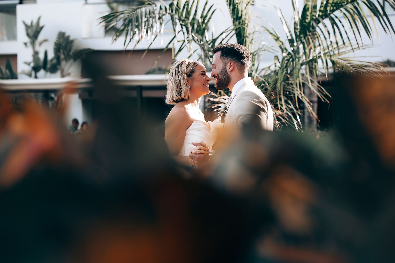 Palm trees frame outdoor wedding ceremony setup with white chairs.