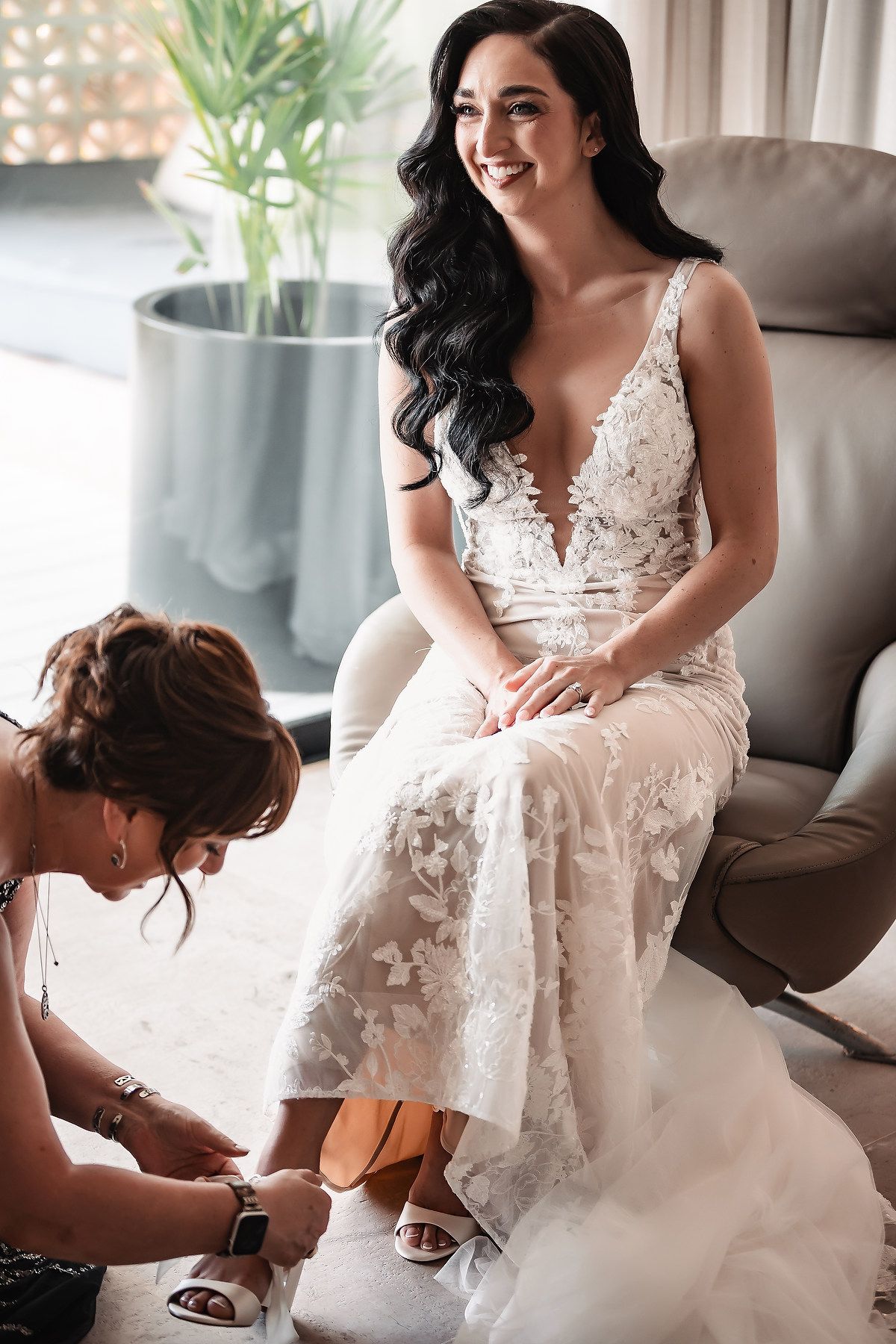 A bride in a white lace wedding dress sits elegantly while getting ready for her special day.