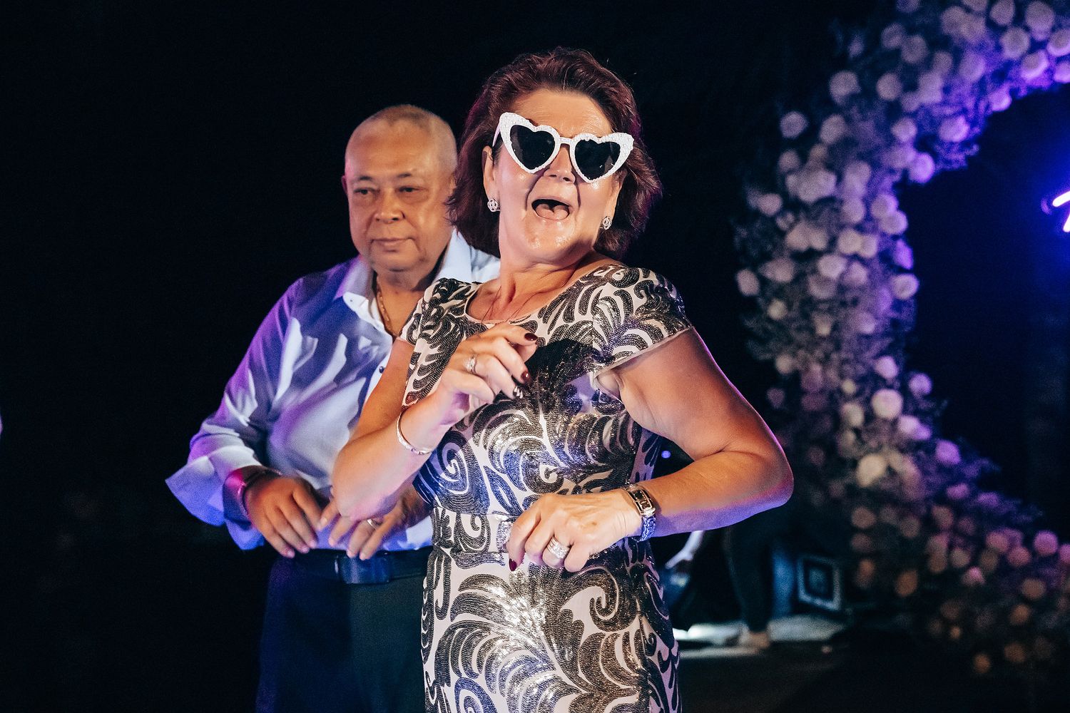 Wedding guests dancing and celebrating at evening reception with purple lighting.