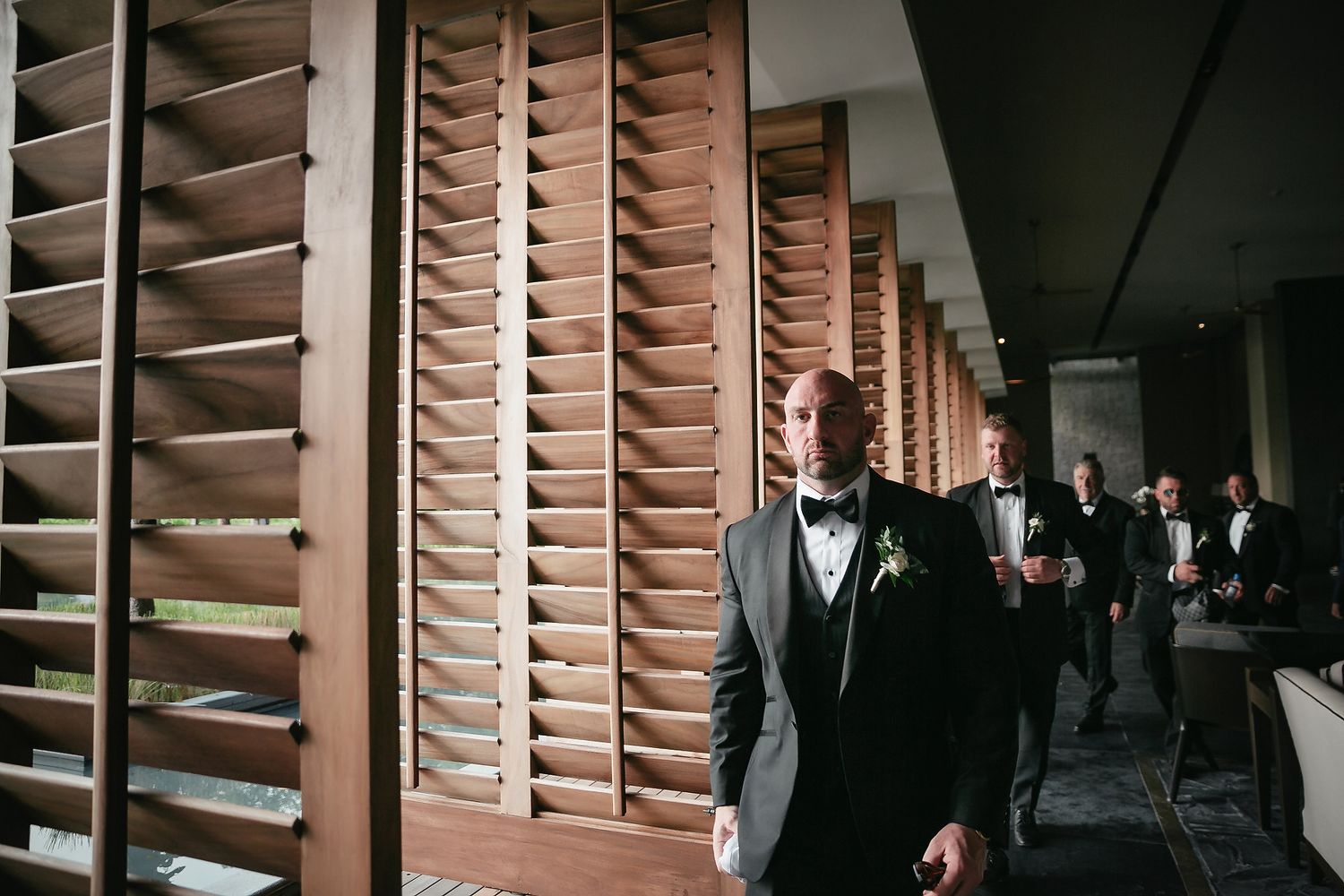 A row of wooden window shutters in a dimly lit hallway with figures walking past.