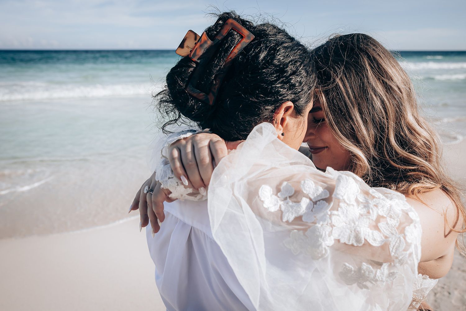Dreamy beachside wedding portraits with white attire against turquoise ocean waves and sandy shoreline.