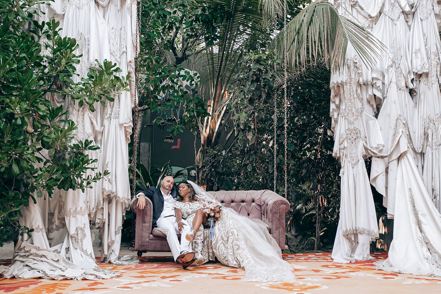 A series of white fabric drapes and greenery create an elegant outdoor wedding ceremony backdrop.