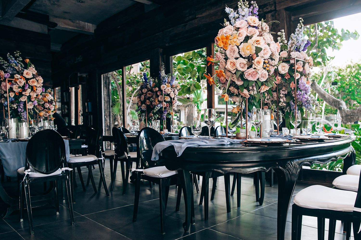 Panoramic view of an outdoor restaurant patio with tables and chairs under a covered area surrounded by lush greenery.