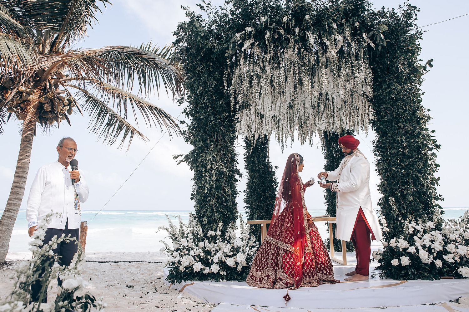 Wide shot of a beachside Indian wedding with tropical palm trees and white decor.