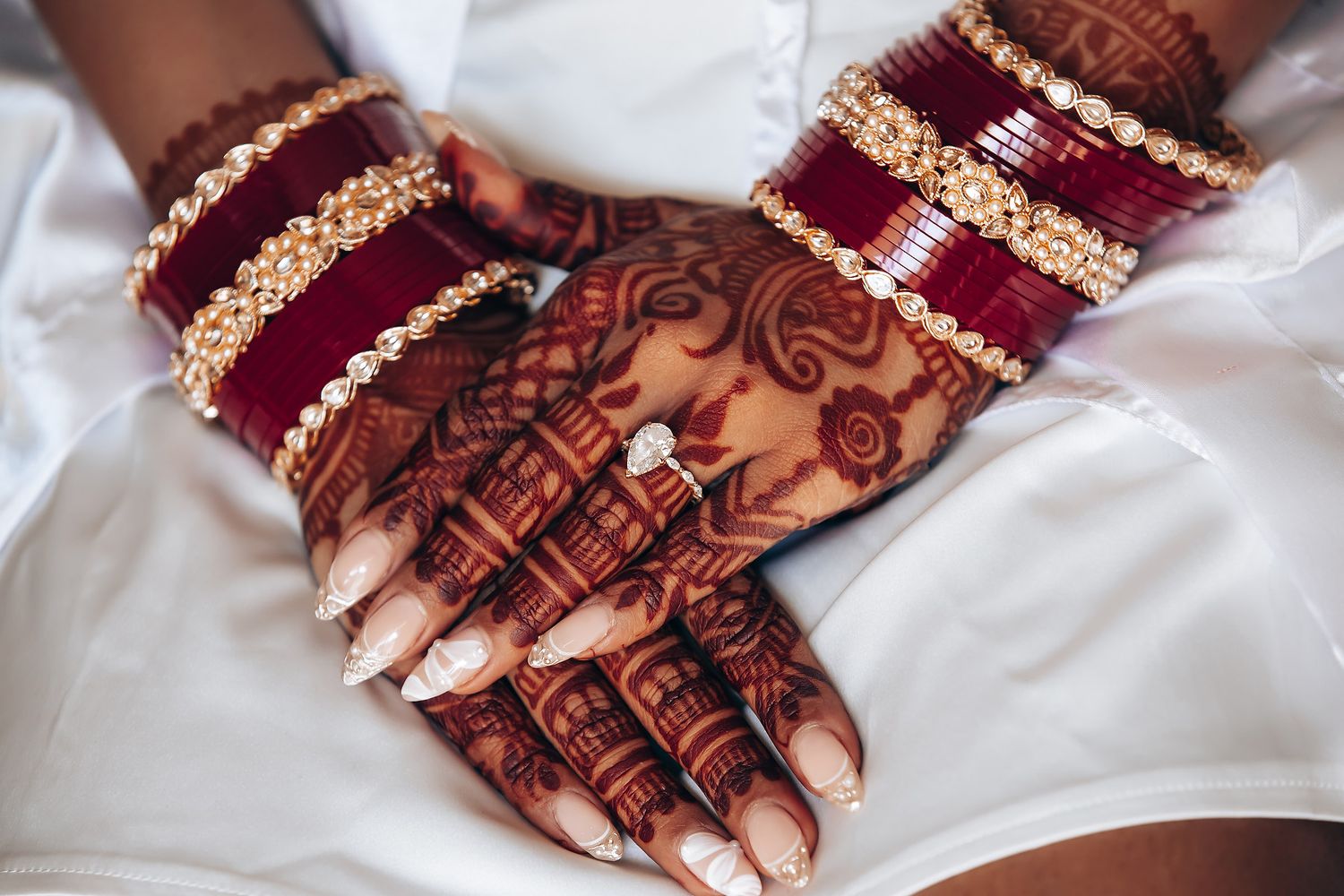 Close-up of intricate henna designs on hands adorned with traditional red and gold bangles.